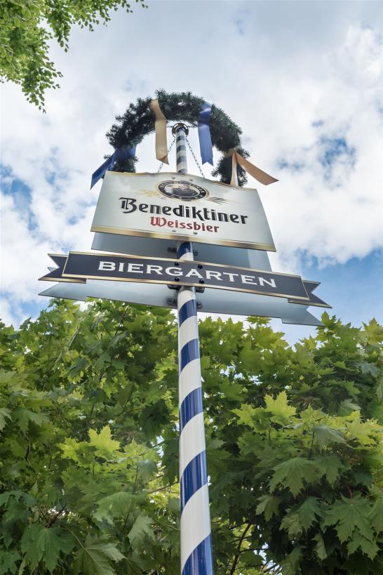 Bild von einem bayrischen Maibaum mit "Biergarten" Schild und Benediktiner Weissbier Werbung
